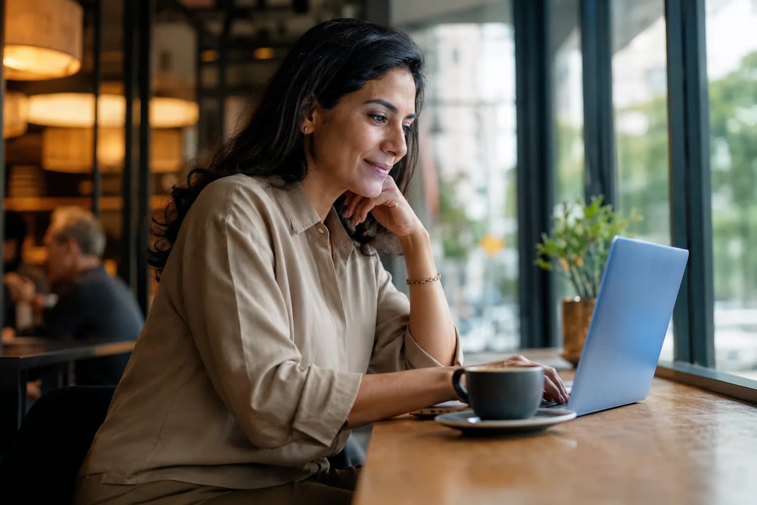 A buyer researching a founder on her laptop in a bright cafe, showing how a thin online presence quietly costs deals the founder never sees.