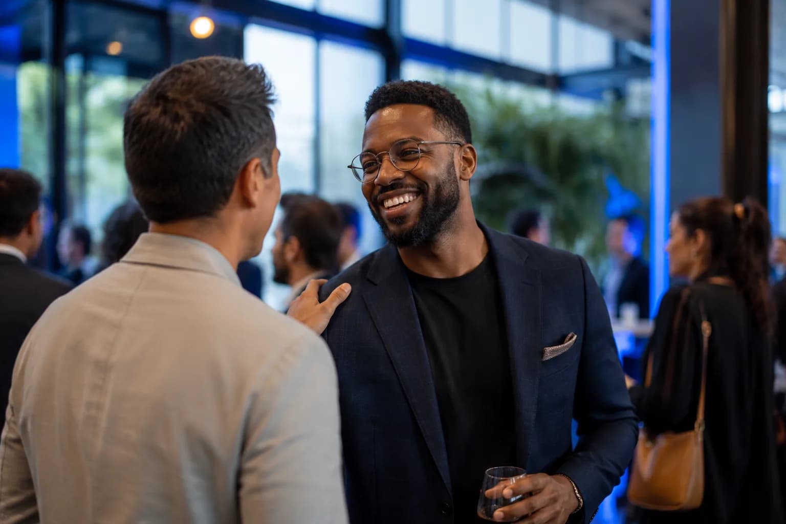 A founder warmly recognized by a peer at a bright networking reception, illustrating the inbound recognition that follows once the authority gap is closed.