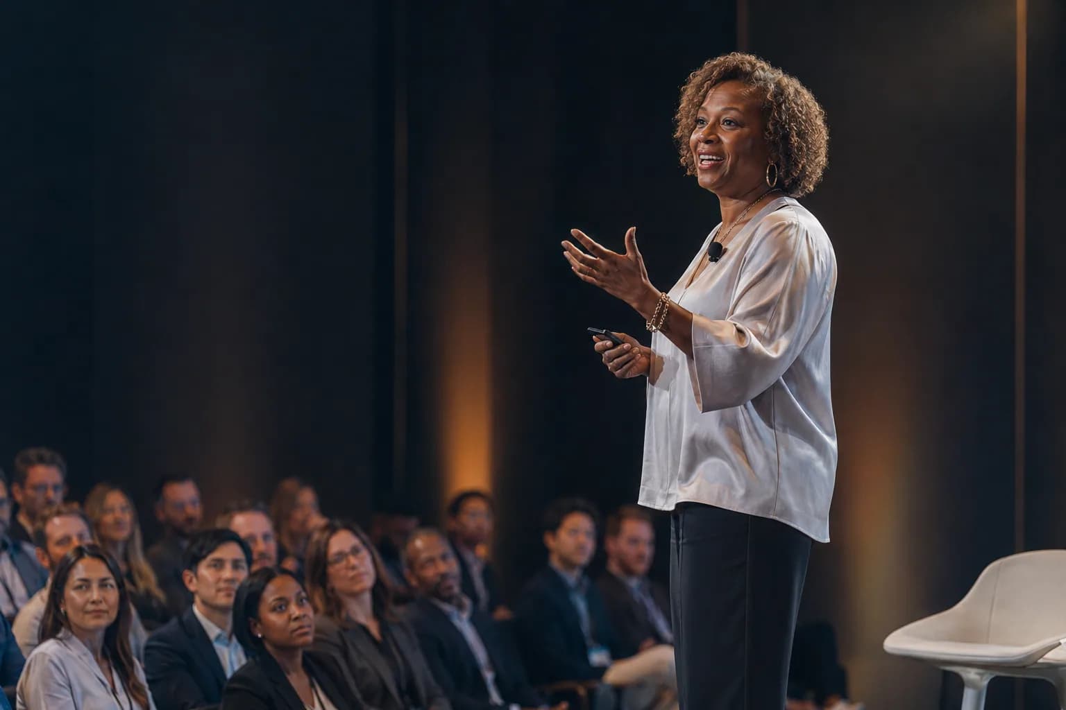 A distinguished researcher energetically presenting to an engaged audience on a modern stage, showing world-class work finally made visible to the market that needed it.