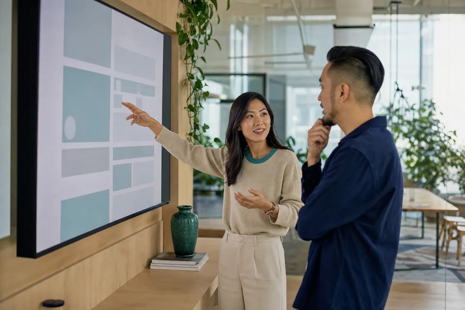 Personal brand website design session where an East Asian female founder reviews an abstract site layout on a large studio display with her designer, building a site that converts authority into pipeline.